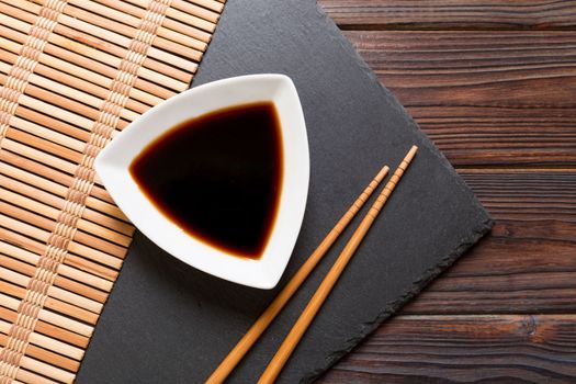 Chopsticks and soy sauce on black stone plate, wooden background with copy space.