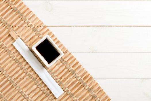 Bamboo mat and soy sauce with sushi chopsticks on white wooden table. Top view with copy space background for sushi. Flat lay.