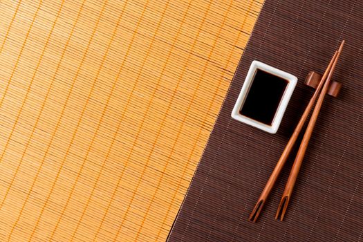 Chopsticks and bowl with soy sauce on two bamboo mat blak and yellow top view with copy space.