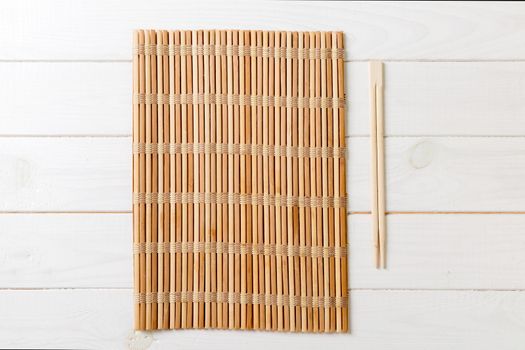 two sushi chopsticks with empty bamboo mat or wood plate on wooden Background Top view with copy stace.