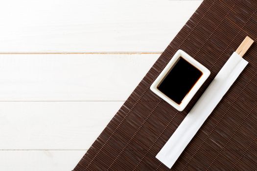 Bamboo mat and soy sauce with sushi chopsticks white on wooden table. Top view with copy space background for sushi. Flat lay