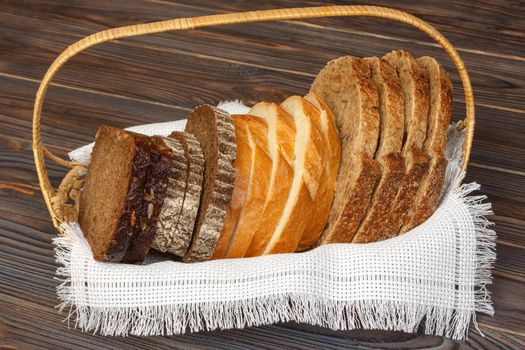 Basket with different kind sliced bread on wooden background.