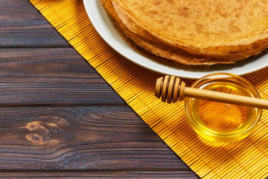 Stack of tasty pancakes with honey in jar on wooden bachground.