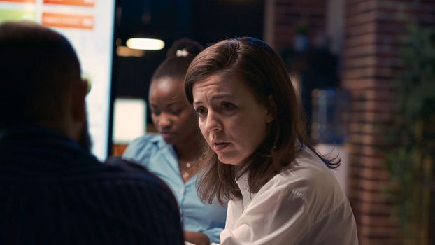 Woman talking with employee in business meeting, sitting at boardroom table. Colleagues discussion, brainstorming, communication in coworking space, office manager speaking close up. Handheld shot.