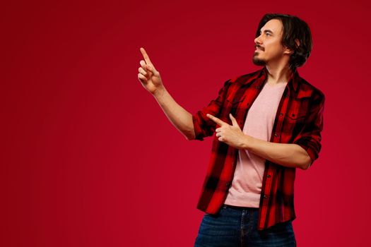 Portrait of a happy bearded man pointing fingers up at copyspace isolated over yellow background