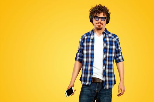 Handsome stylish man in hipster plaid shirt and sunglasses posing over yellow background