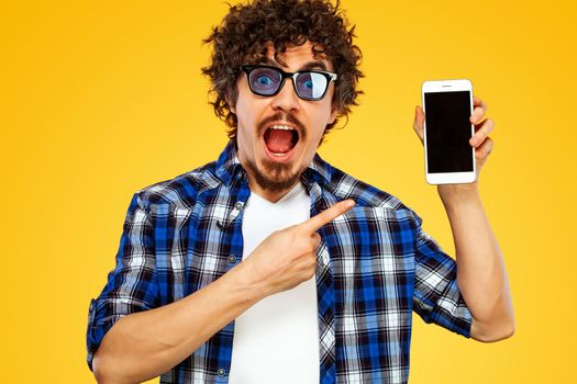 Handsome stylish man in hipster plaid shirt and sunglasses posing over yellow background