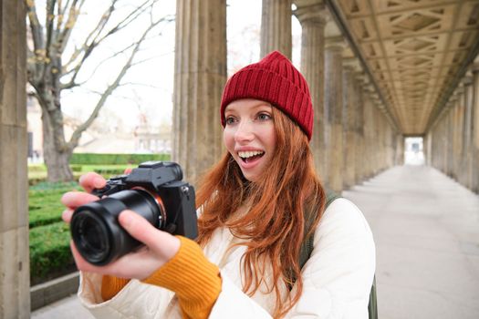 Smiling tourist photographer, takes picture during her trip, holds professional camera and makes photos. Copy space