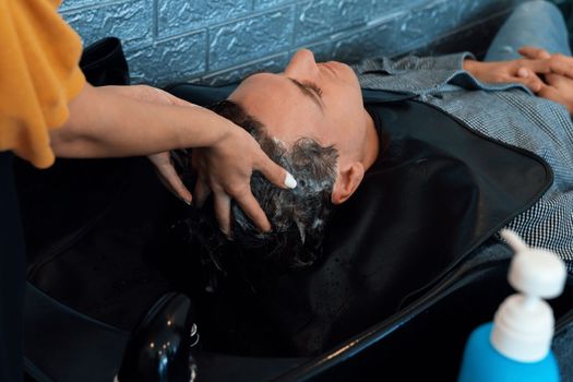 Closeup caucasian man getting hair wash by professional hairdresser with shampoo feels relax and comfortable . Qualified hairdresser with her barbershop, salon providing haircare concept.