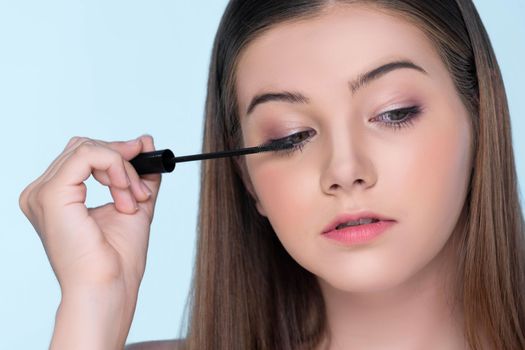 Closeup portrait of young charming applying makeup eyeshadow on her face with brush, mascara with flawless smooth skin for beauty concept.