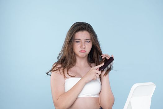 Beautiful girl feel sad, worry about her damaged hair with isolated background. Concept of dry lifeless hair. Young charming girl hold her tangled hair and look at it with worried expression.