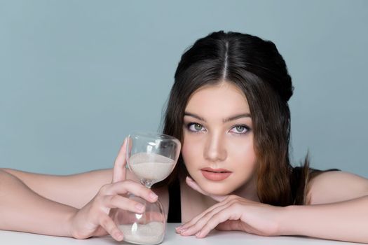 Concept of skincare and anti-aging beauty care with charming young plum girl closeup portrait holding hourglass on isolated background. Fresh and healthy face skin girl with sand glass for cosmetology