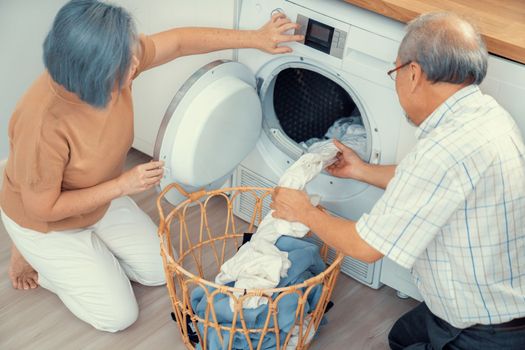 Senior couple working together to complete their household chores at the washing machine in a happy and contented manner. Husband and wife doing the usual tasks in the house.