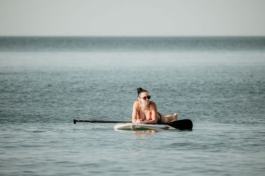 Sea woman sup. Silhouette of happy middle aged woman in rainbow bikini, surfing on SUP board, confident paddling through water surface. Idyllic sunset. Active lifestyle at sea or river