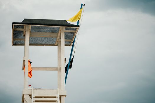 Empty white lifeguard tower with a yellow flag on the beach in windy weather. Beach lifeguard tower with yellow flag indicator. Nobody. Holiday recreation concept
