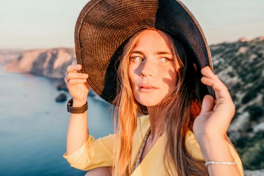 Portrait of happy young woman wearing summer black hat with large brim at beach on sunset. Closeup face of attractive girl with black straw hat. Happy young woman smiling and looking at camera at sea