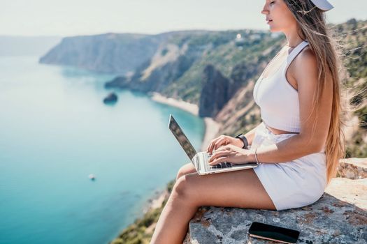 Digital nomad, Business woman working on laptop by the sea. Pretty lady typing on computer by the sea at sunset, makes a business transaction online from a distance. Freelance remote work on vacation