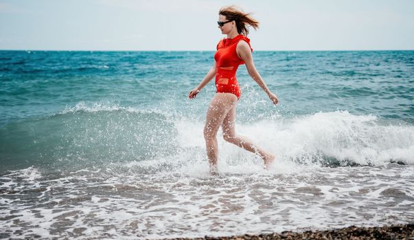 Young happy woman walks carefree on the seaside. Happy lady in red bikini. Portrait beautiful young woman relax smile around beach sea ocean in holiday vacation travel trip.