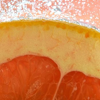 Close-up view of the red grapefruit slice in water background. Texture of cooling fruit drink with macro bubbles on the glass wall. Flat design.