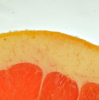 Close-up of a grapefruit slice in liquid with bubbles. Slice of red ripe grapefruit in water. Close-up of fresh grapefruit slice of red on white background.