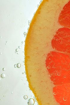 Close-up of juicy grapefruit slice on white background. Slice of red grapefruit in sparkling water on white background, close-up. Vertical macro image.