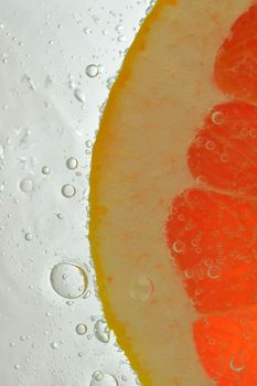 Close-up of juicy grapefruit slice on white background. Slice of red grapefruit in sparkling water on white background, close-up. Vertical macro image.