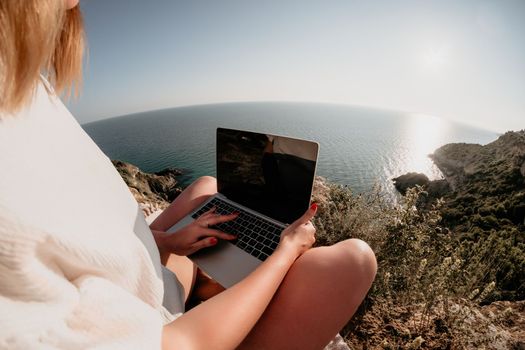 Woman sea laptop. Business woman in yellow hat working on laptop by sea. Close up on hands of pretty lady typing on computer outdoors summer day. Freelance, digital nomad, travel and holidays concept.