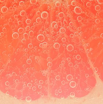 Close-up of a grapefruit slice in liquid with bubbles. Slice of red ripe grapefruit in water. Close-up of fresh grapefruit slice covered by bubbles.