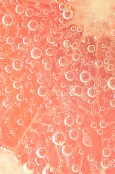 Close-up of a grapefruit slice in liquid with bubbles. Slice of red ripe grapefruit in water. Close-up of fresh grapefruit slice covered by bubbles.