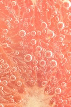 Slice of grapefruit in sparkling water. Grapefruit slice covered by bubbles in carbonated water. Grapefruit slice in water with bubbles.