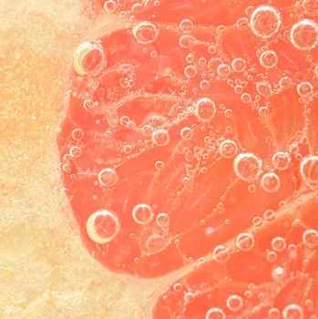 Slice of red grapefruit in water on white background. Grapefruit close-up in liquid with bubbles. Slice of red ripe grapefruit in water. Macro image of fruit in water.