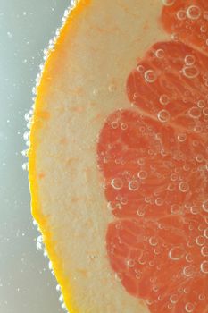 Close-up of fresh grapefruit slice on white background. Slice of red grapefruit in sparkling water on white background, close-up. Vertical image.