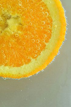 Close-up of fresh orange slice on white background. Slice of orange in sparkling water on white background, close-up. Horizontal image.ice in liquid with bubbles. Slice of orange fruit in water. Close-up of fresh orange fruit slice covered by bubbles. Vertical image.