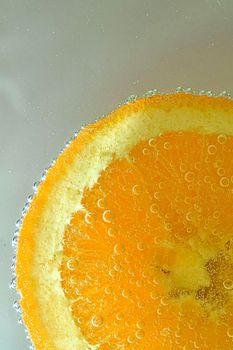 Close-up view of the orange fruit slice in water background. Texture of cooling fruit drink with macro bubbles on the glass wall. Flat design. Vertical image.