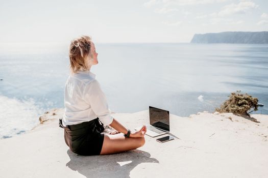 Happy girl doing yoga with laptop working at the beach. beautiful and calm business woman sitting with a laptop in a summer cafe in the lotus position meditating and relaxing. freelance girl remote work beach paradise