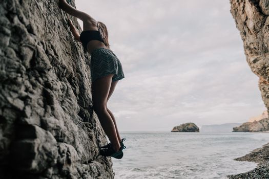 A girl climbs a rock. The athlete trains in nature. Woman overcomes difficult climbing route. Extreme hobby. Tourist woman rock climber hiking on mountains rocks over beautiful sea coast