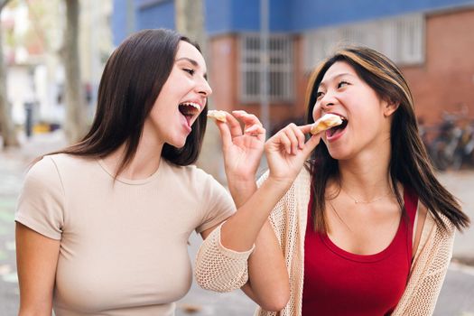 portrait of a couple of young women sharing some sweet buns sitting in a city park, concept of friendship and love between people of the same sex