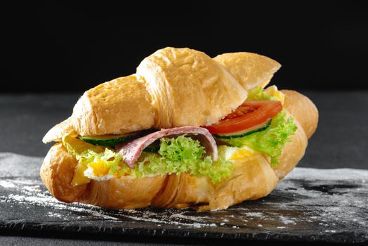 Croissant sandwich with sausage on a dark background.