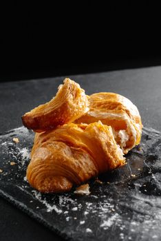 Close-up of croissants on a dark background. One croissant broken into pieces.