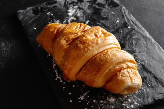 Large croissant on black background. Fresh and delicious French pastries, bakery concept, close-up image.