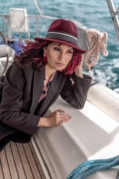 Portrait of a woman on a yacht in the sea, she has burgundy curly hair, looks to the side