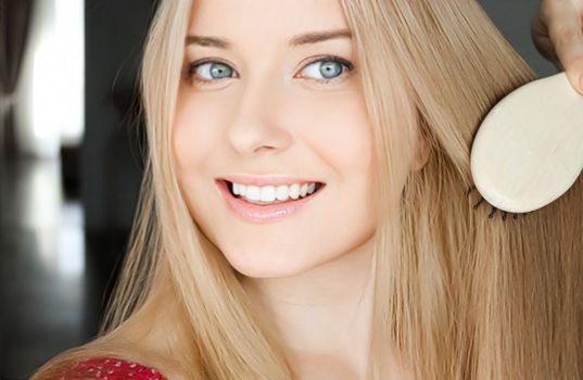 Beautiful happy woman combing her long blond hair.