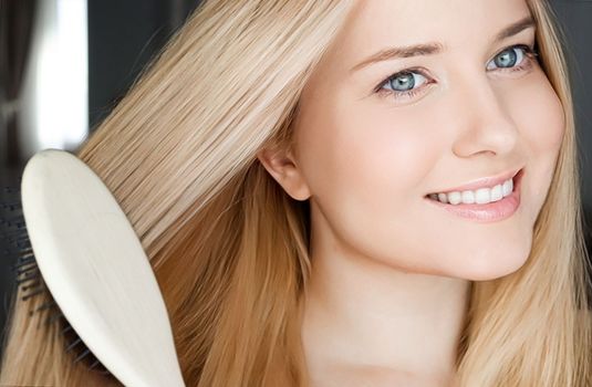 Beautiful happy woman combing her long blond hair.