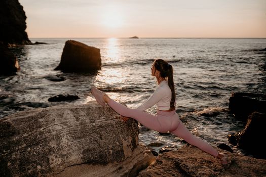 Young woman with black hair, fitness instructor in pink sports leggings and tops, doing pilates on yoga mat with magic pilates ring by the sea on the beach. Female fitness daily yoga concept