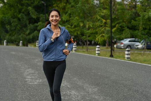 Shot of asian woman in sportswear and earphones jogging in public park. Fitness, sport and healthy lifestyle concept.