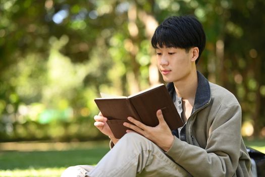 Image of calm asian college student reading books against beautiful nature view background. Education and lifestyle concept.