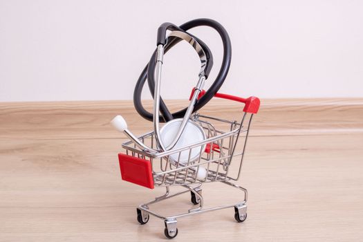 Stethoscope in shopping cart on wooden background close up