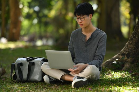 Young man sitting on grass in the city park and using laptop. Education, technology lifestyle concept.