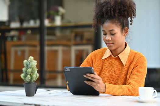 Smiling African American woman working remotely, using digital tablet in outdoor coffee shop.