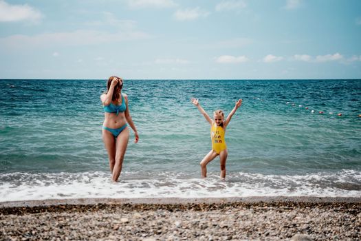 Happy loving family mother and daughter having fun together on the beach. Mum playing with her kid in holiday vacation next to the ocean - Family lifestyle and love concept.